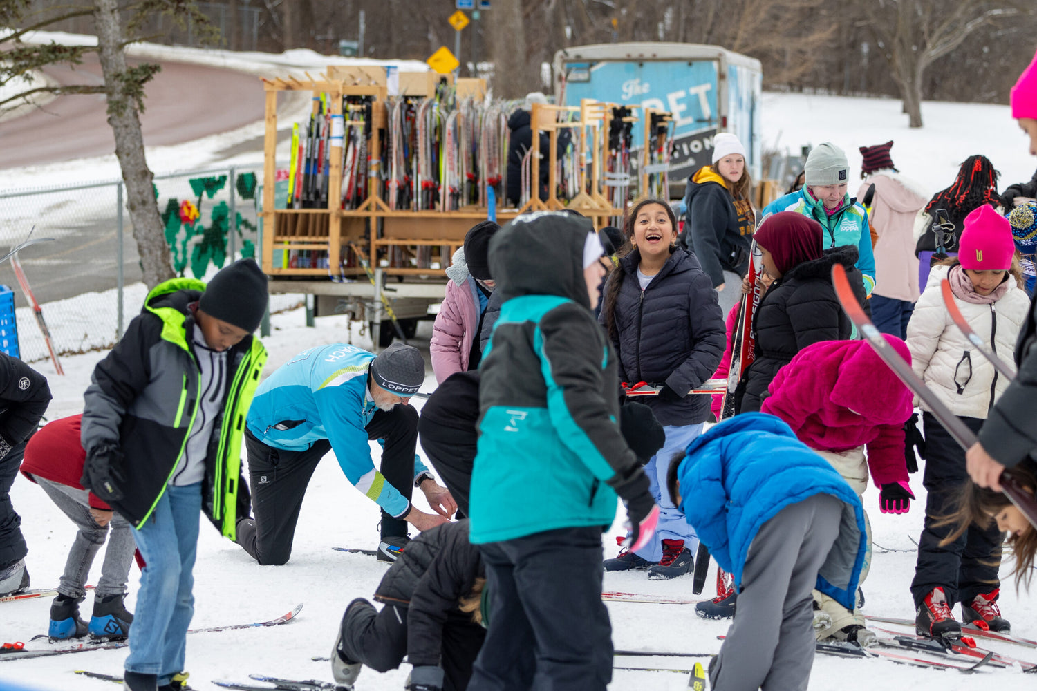Group of people, including children, preparing for skiing in a snowy outdoor setting.