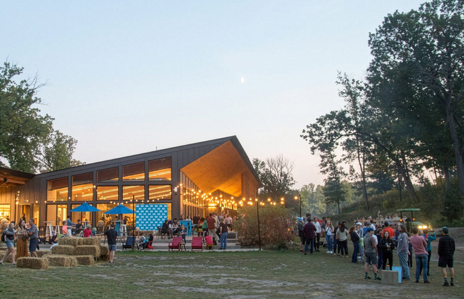 Outdoor event at a modern building with people gathered around, trees in the background