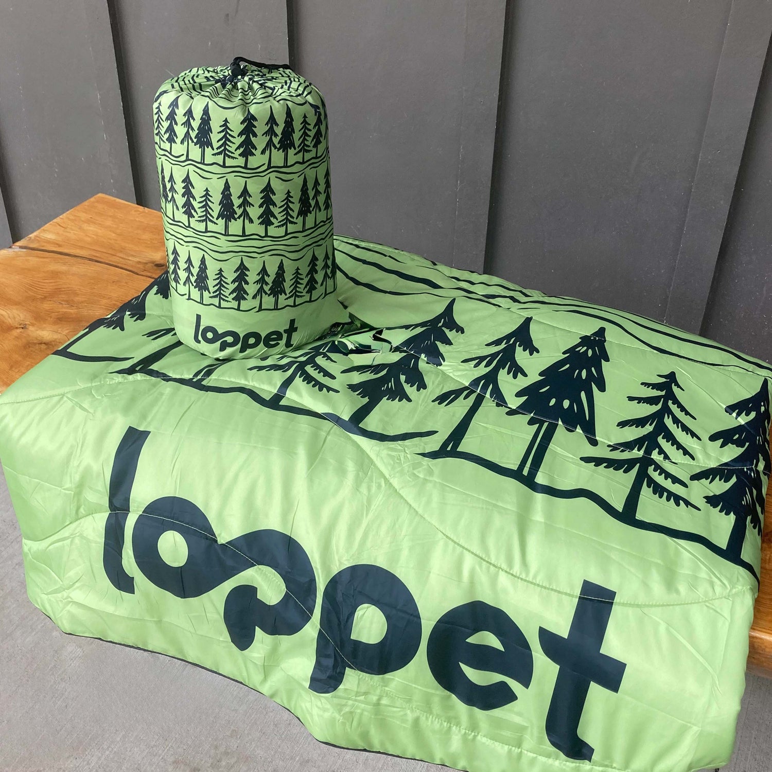 Green blanket bag with tree pattern and 'loppet' branding on a wooden surface.